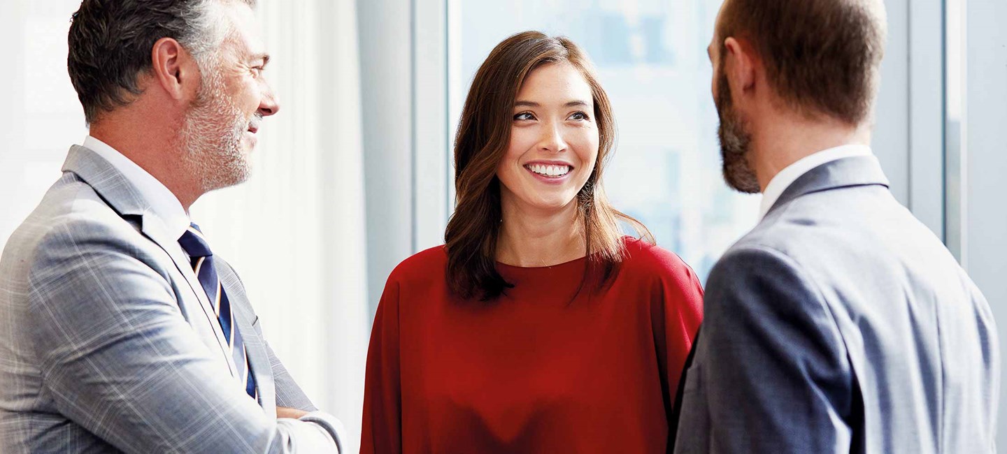 Two men in suits chatting to a lady wearing a red jumper