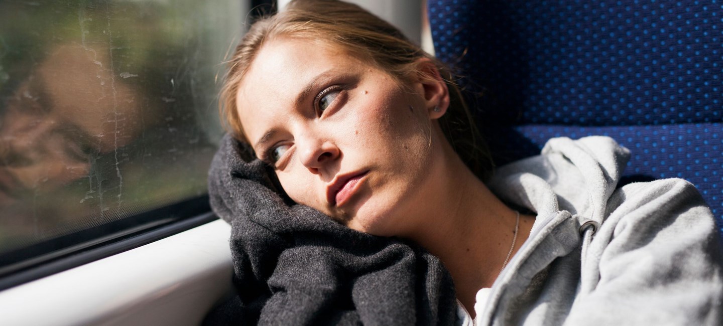 Woman staring out of a train window with a sombre look on her face. 