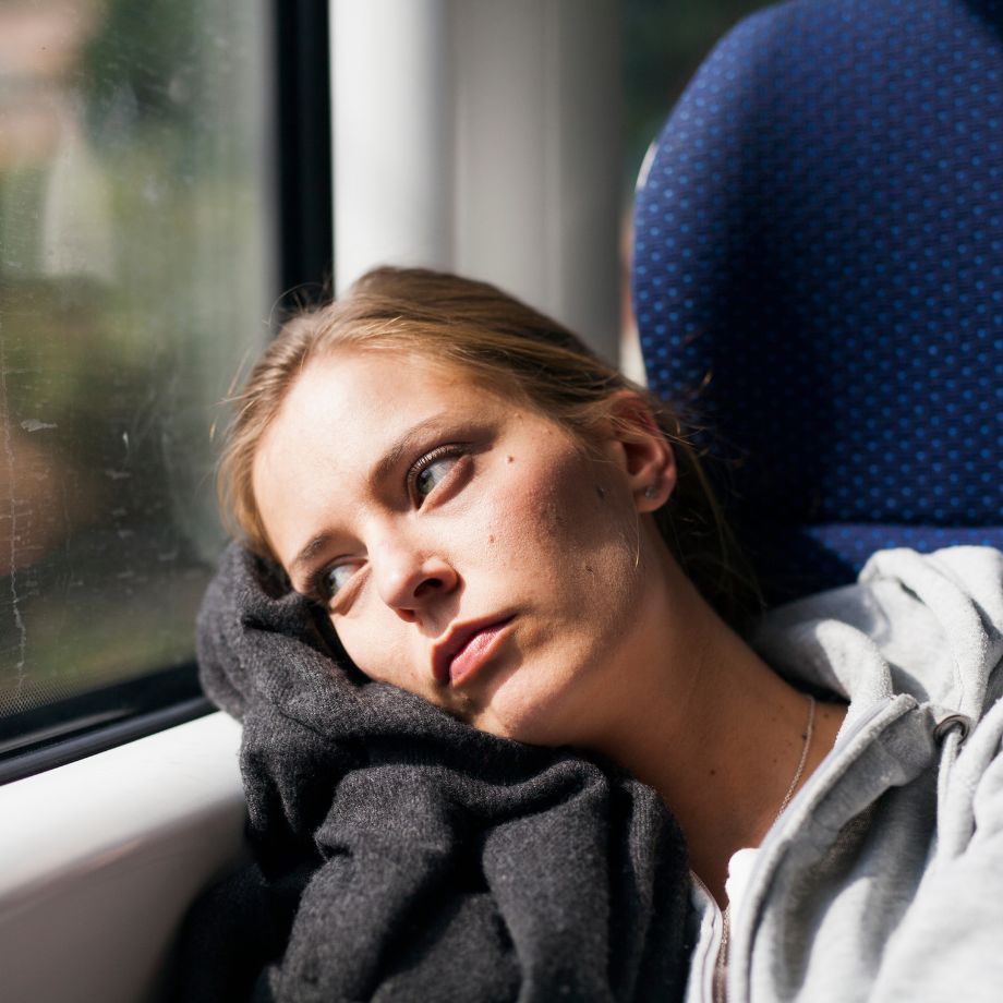 Woman staring out of a train window with a sombre look on her face. 